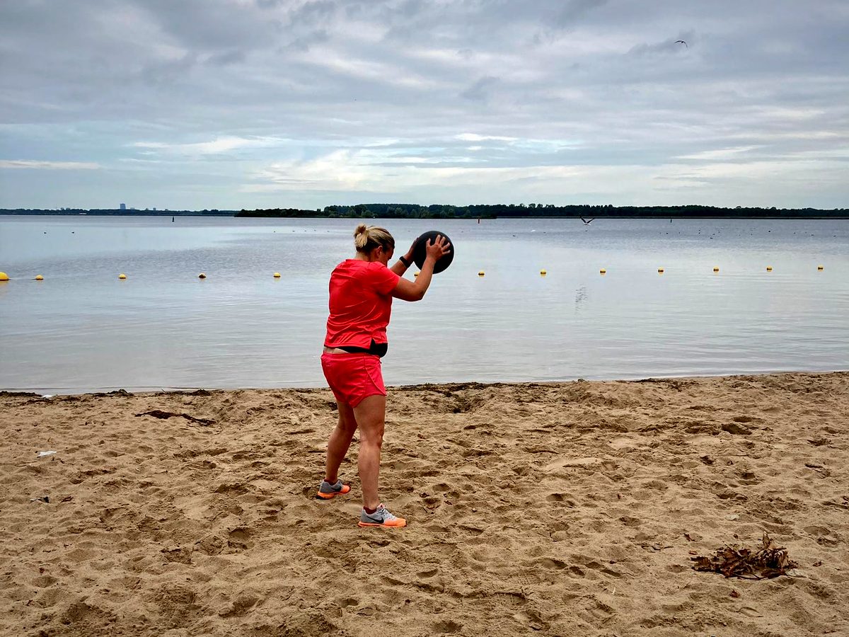 Iemand houdt een medicinebal boven het hoofd op een strand