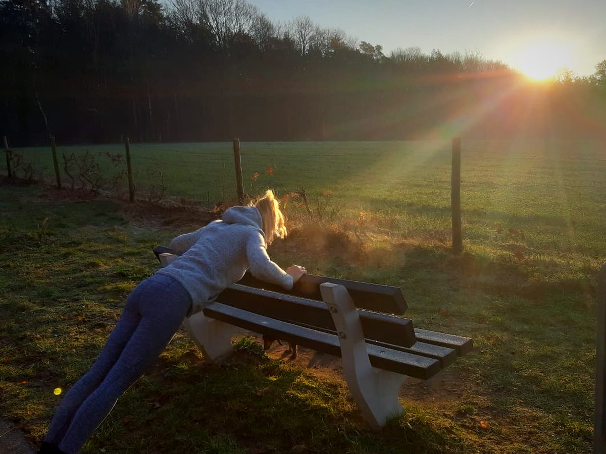 Iemand doet opdrukoefeningen tegen een picknickbank in het late zonlicht