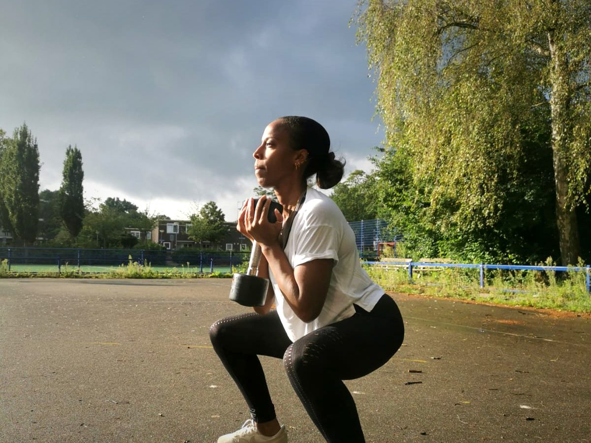 Iemand doet een diepe kniebuiging met een kettlebell op een grijze dag