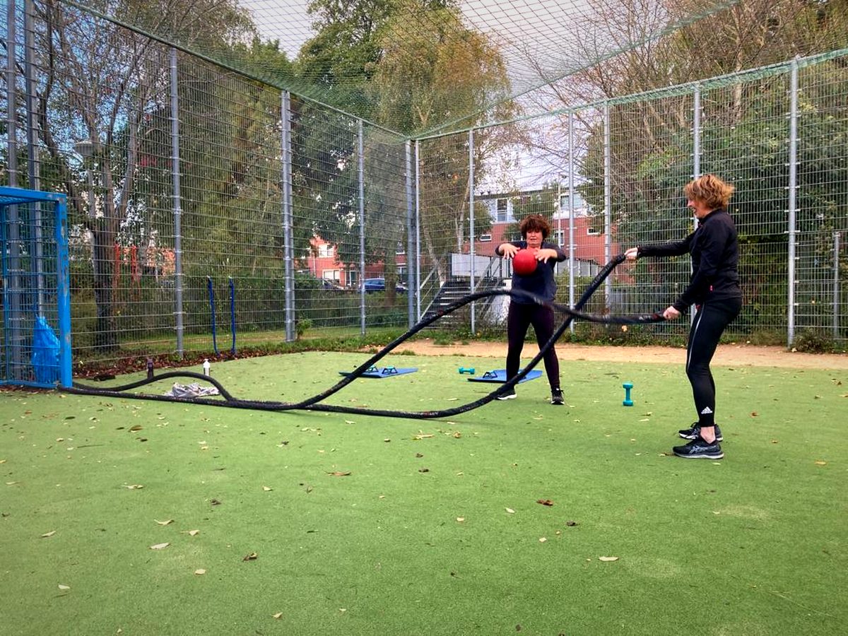 Twee mensen trainen met zware touwen op een kunstgrasveld